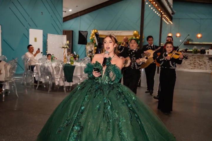 Quinceañera in emerald gown singing with mariachi band at our Orem, Utah event venue