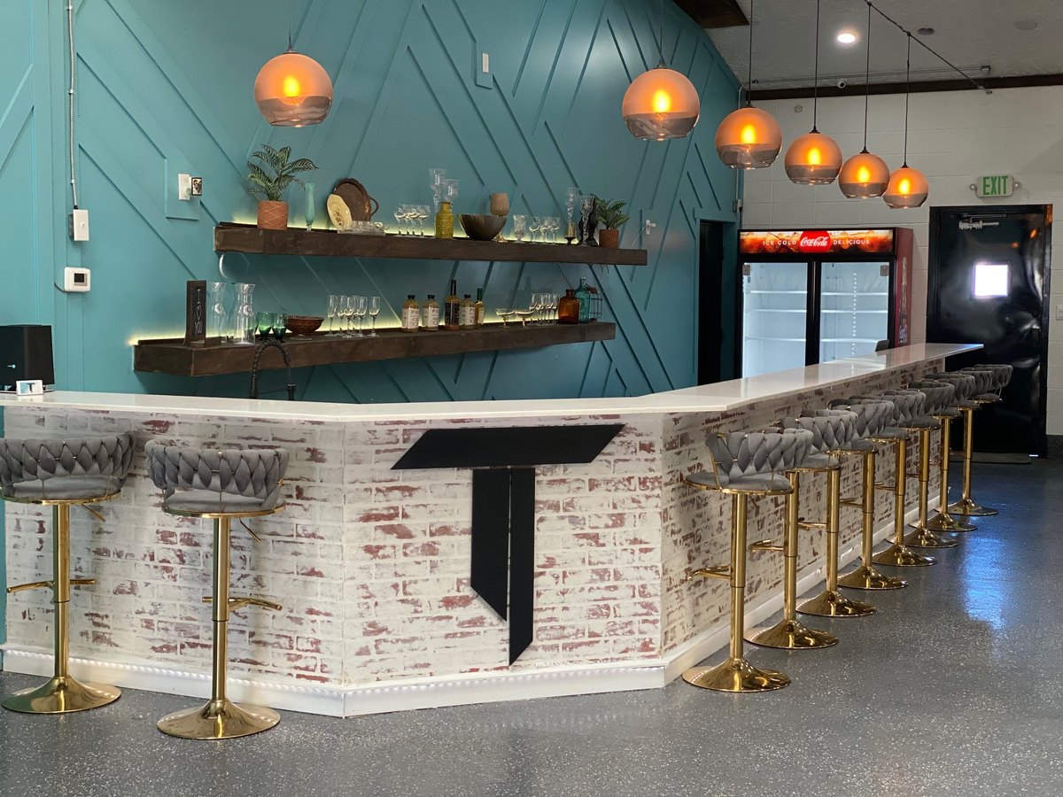 The bar with gold stools and backlit shelves on the blue accent wall at our Orem venue