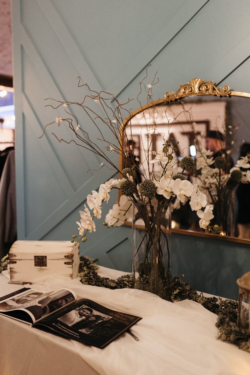 A gold mirror with dried florals and a guestbook on the blue accent wall at our Orem event venue